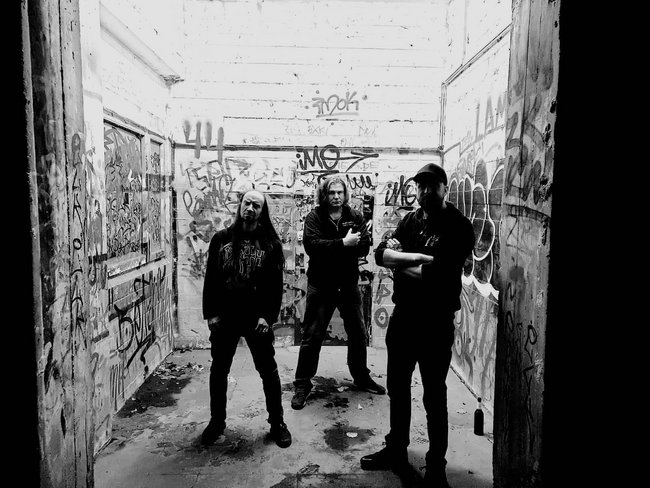 Auf dem Bild sieht man die Band Dread Polaris. Sie stehen in einem Bunker. Die Wände sind mit Graffiti besprüht, der Boden ist dreckig und es steht eine Sektflasche auf dem Boden.